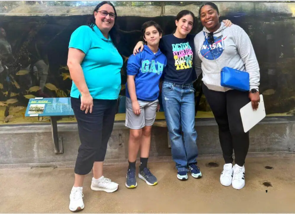 Four people pose happily in front of an aquarium.