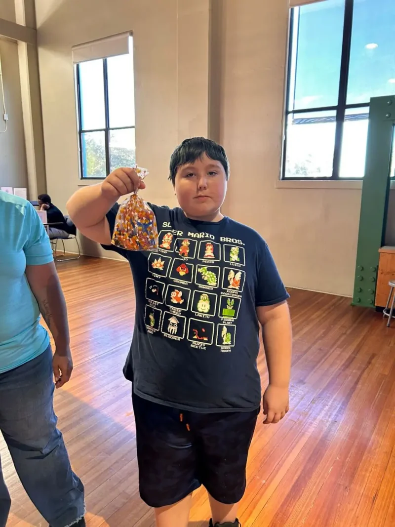 A young person stands indoors on a wooden floor