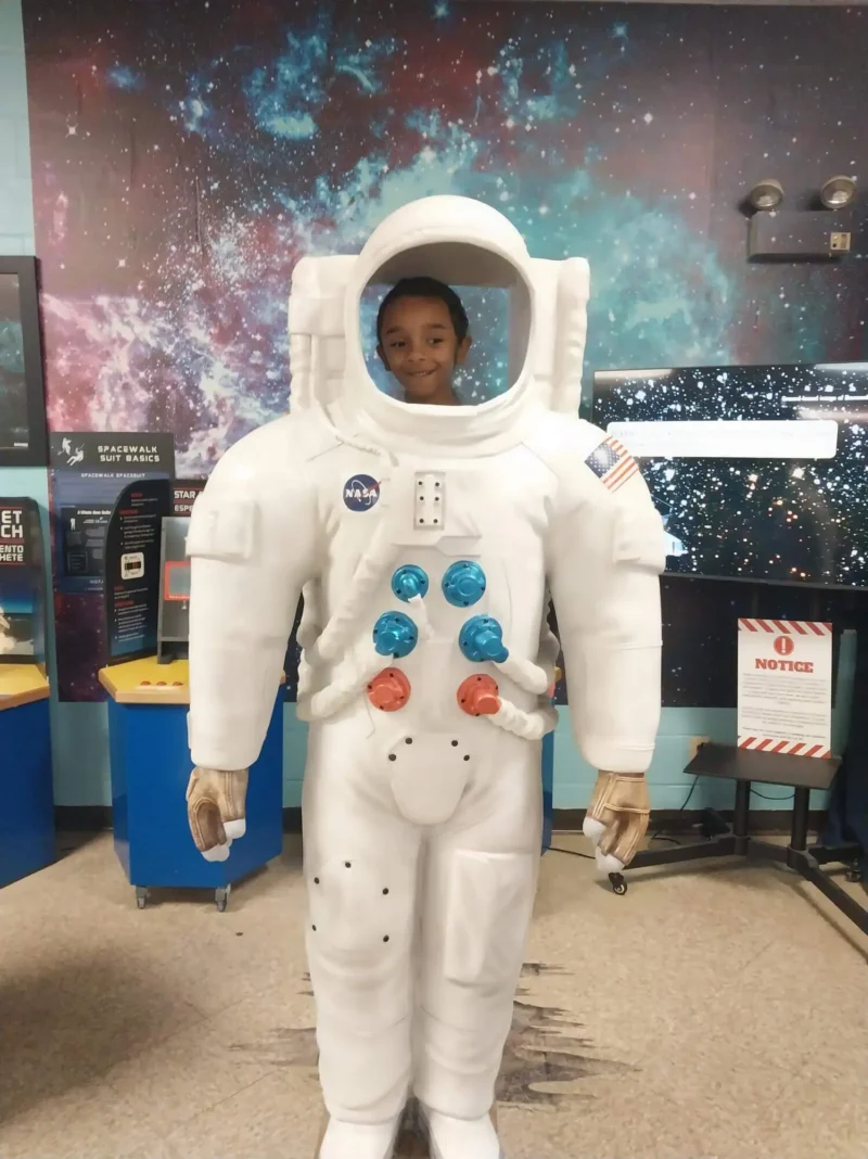 Child smiling from an astronaut suit cutout at a space exhibit