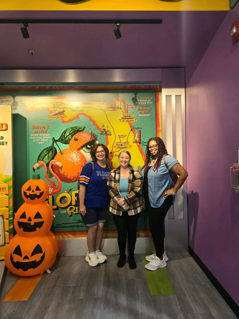 Three woman standing next to three pumpkins