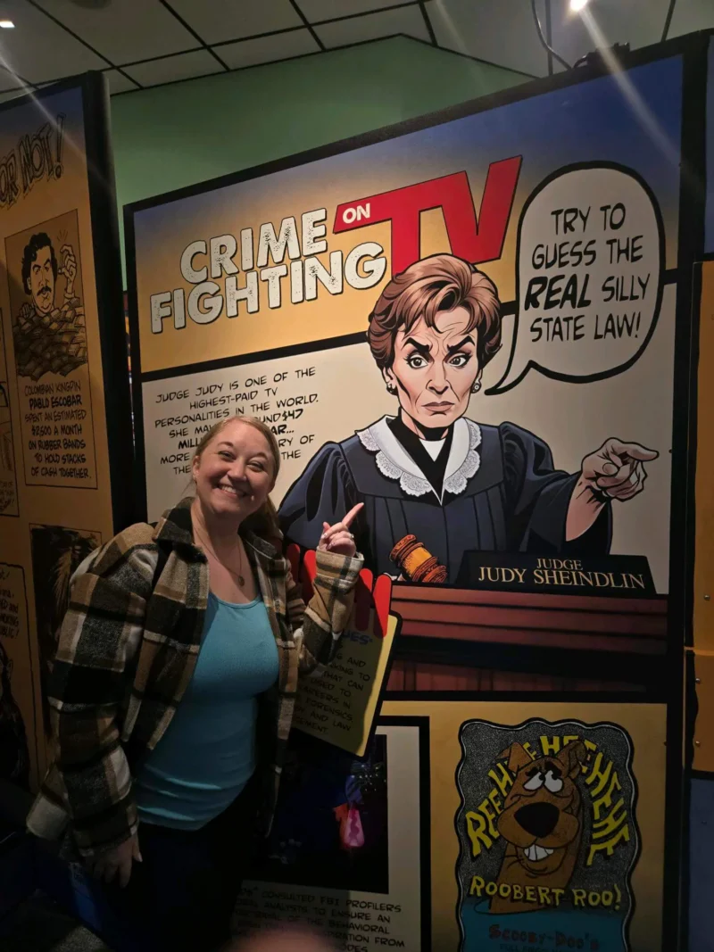 A woman smiles and points to a cartoon mural of a stern judge.